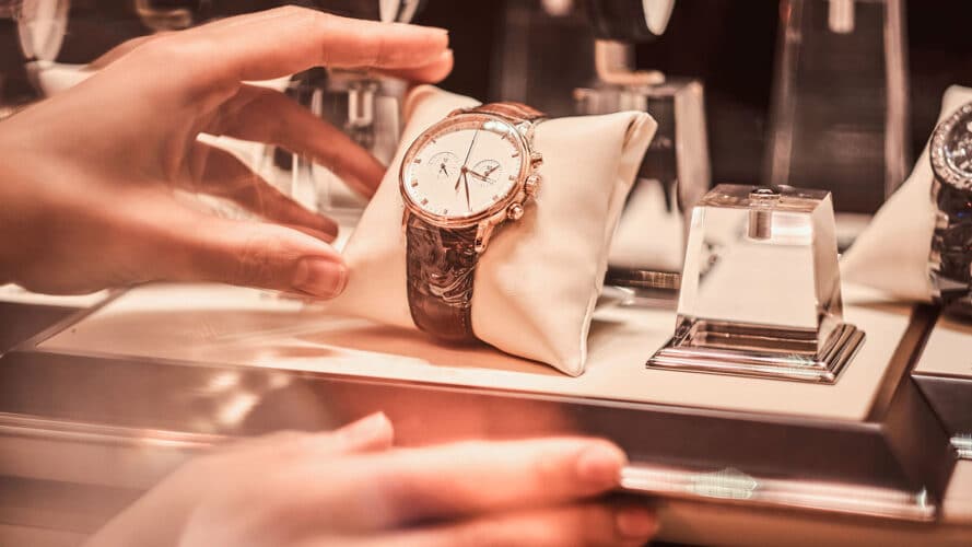 Hand platziert Uhr auf kleinem Präsentationskissen im Schaufenster als symbolische Darstellung von Onsite Merchandising.