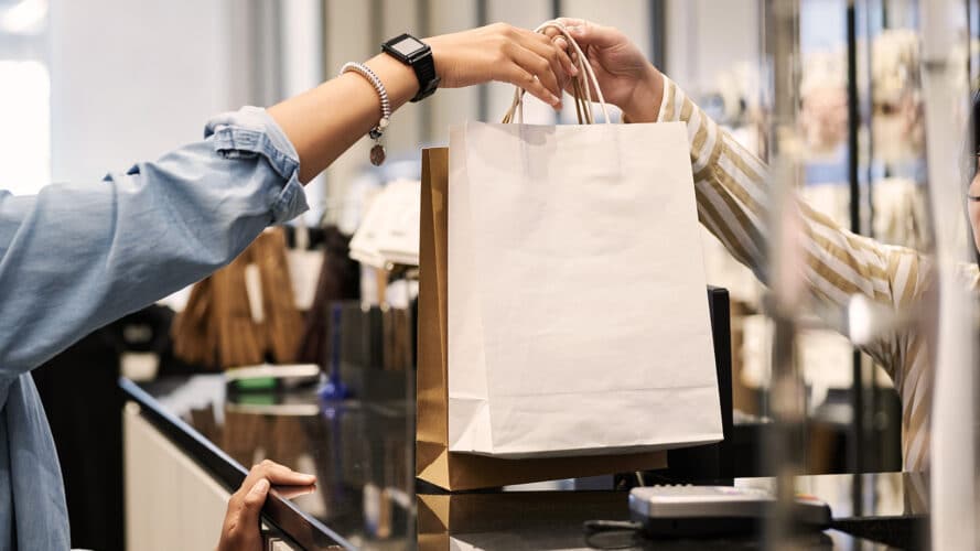 Eine Verkäuferin überreicht einer Kundin eine Einkaufstasche an der Ladentheke – symbolisch für erfolgreiche Conversion-Optimierung.