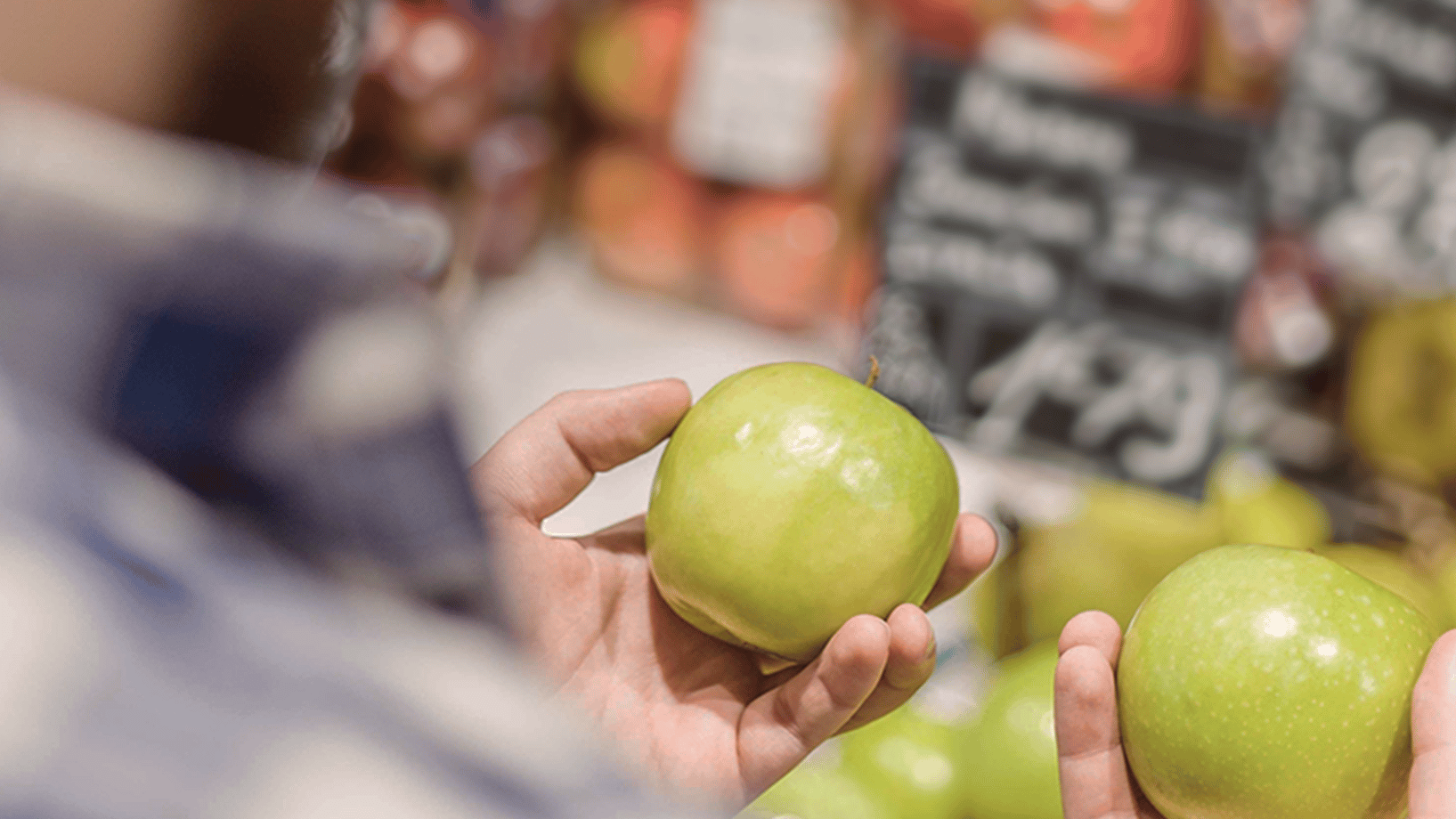Dieses Bild zeigt einen Kunden an der Obsttheke, der sich zwichen zwei scheibar gleichen Äpfeln entscheidet.