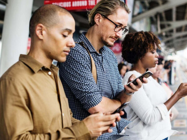 Big Data im E-Commerce wird über drei Personen visualisiert, die ein Smartphone am Gleis eines Bahnhofs nutzen.