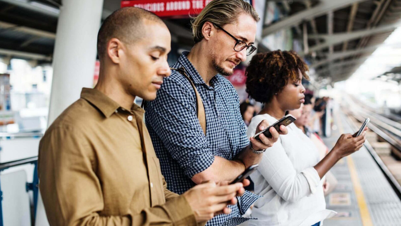 Big Data im E-Commerce wird über drei Personen visualisiert, die ein Smartphone am Gleis eines Bahnhofs nutzen.