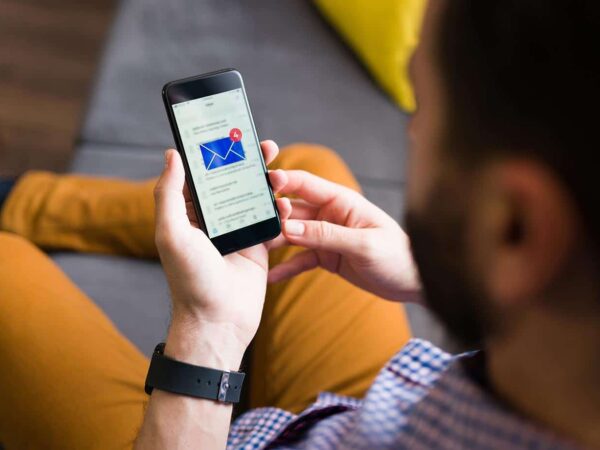 Das Bild zeigt einen Mann mit einem Smartphone in der Hand, auf dem ein E-Mail-Postfach geöffnet ist und neue Nachrichten vorhanden sind.
