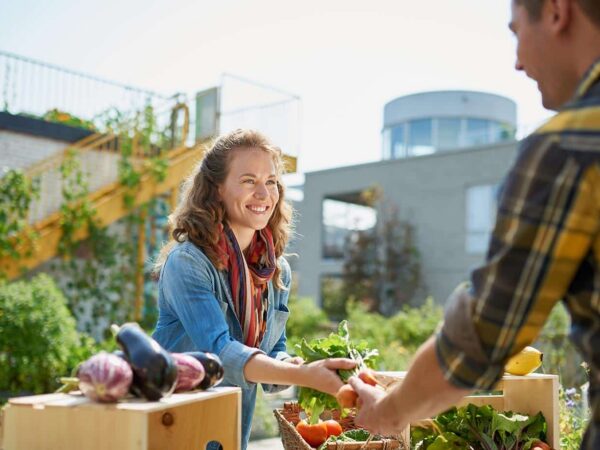 Das Bild zeigt einen Marktstand, bei dem eine Person Möhren kauft.