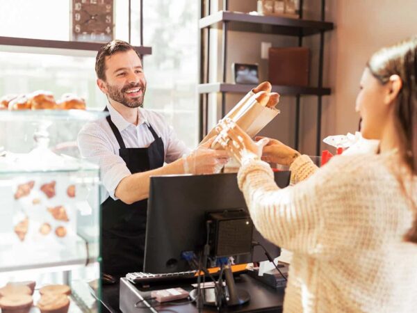 Eine Frau kauft bei einem Bäcker Baguettes.
