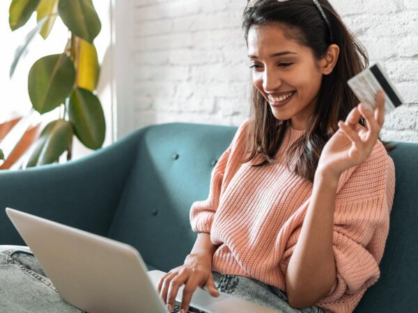 Das Bild zeigt eine Frau mit einem Laptop und einer Kreditkarte in der Hand.
