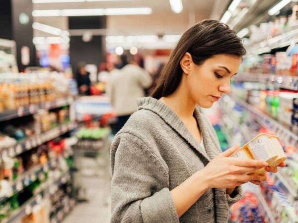 Eine Frau sieht sich in einem Supermarkt ein Produkt genauer an und liest die Produktbeschreibung.