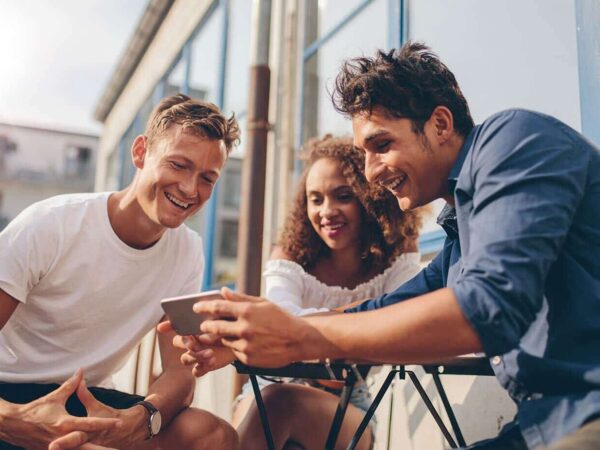 Das Bild zeigt drei Personen, die auf ein Smartphone schauen.