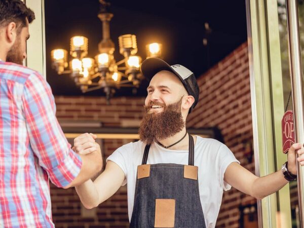 Ein Ladenbesitzer begrüßt seinem Kunden an der Tür des Geschäfts.
