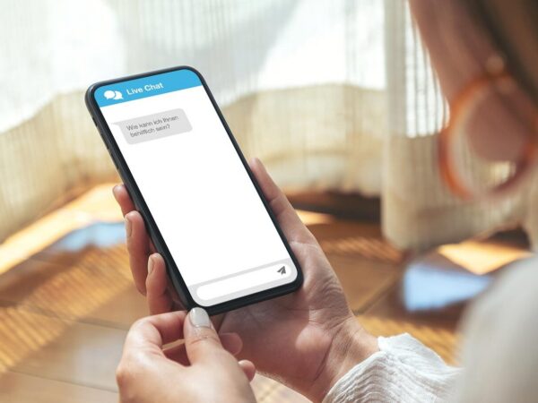 Eine Frau hält ein Smartphone in der Hand, auf dem ein Live-Chat-Fenster geöffnet ist.