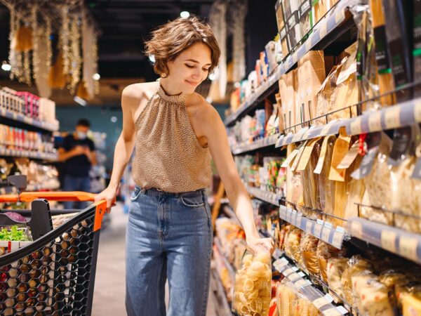 Eine Frau im Supermarkt steht zwischen zwei Regalen mit Pasta und Soßen, ein Beispiel für sinnvolles Category Management.
