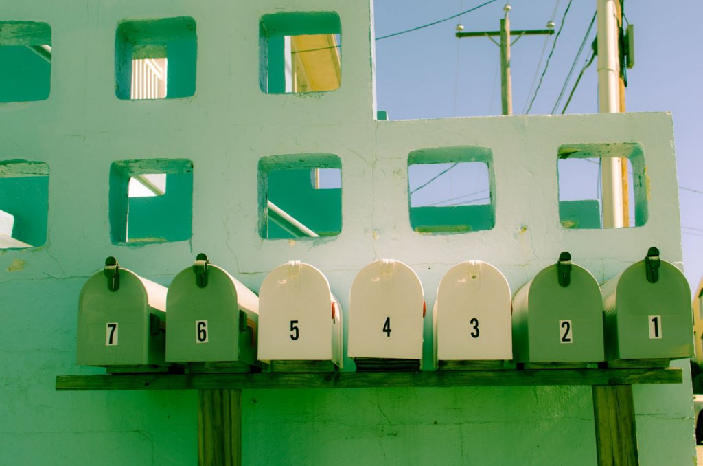 Von 1 bis 7 nummerierte, grüne und weiße Briefkästen sind vor einer Mauer aufgestellt als Symbol für relevanten Inhalt in der E-Mail