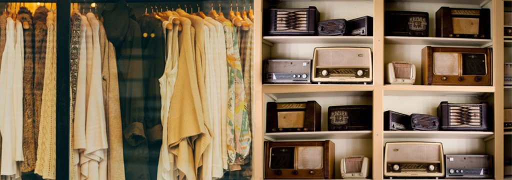 In einem Schrank hängt in der einen Hälfte Kleidung, in der anderen stehen in 8 Fächer geordnet verschiedene alte Radios. Personalisierung im Branchenvergleich, Modebranches vs. Elektronikbranche.