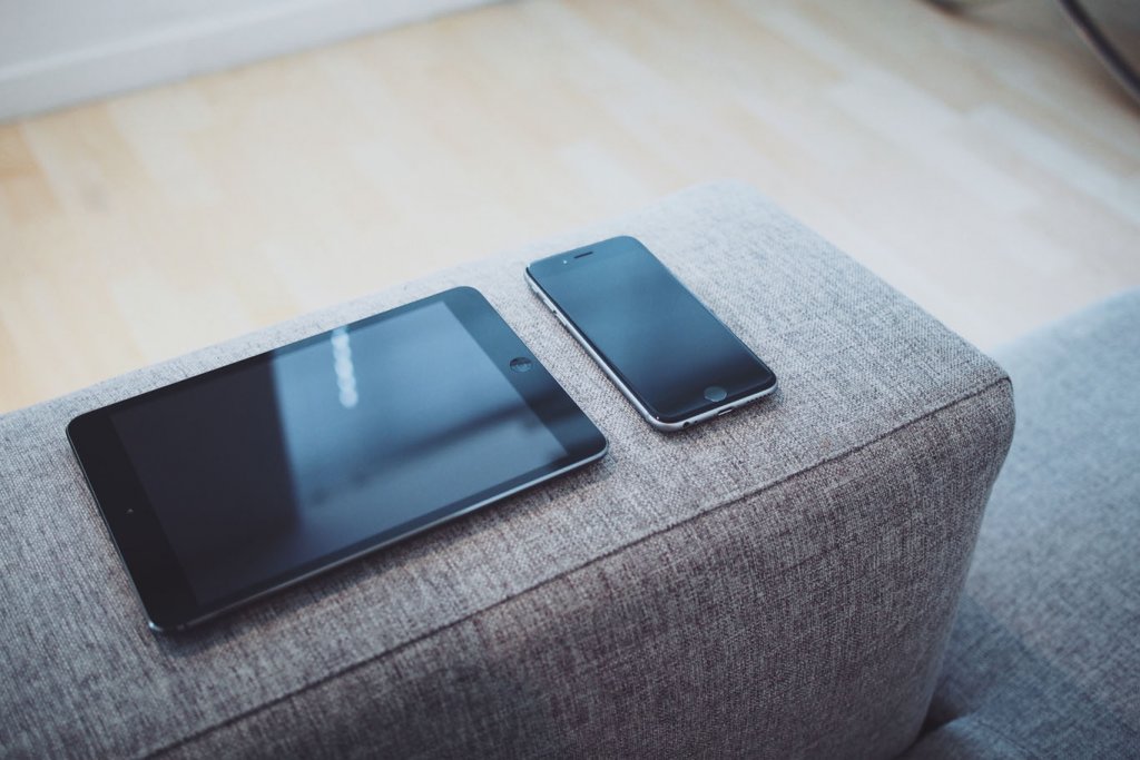 Ein Smartphone und ein Tablet liegen ordentlich nebeneinander auf der Armlehne einer Couch