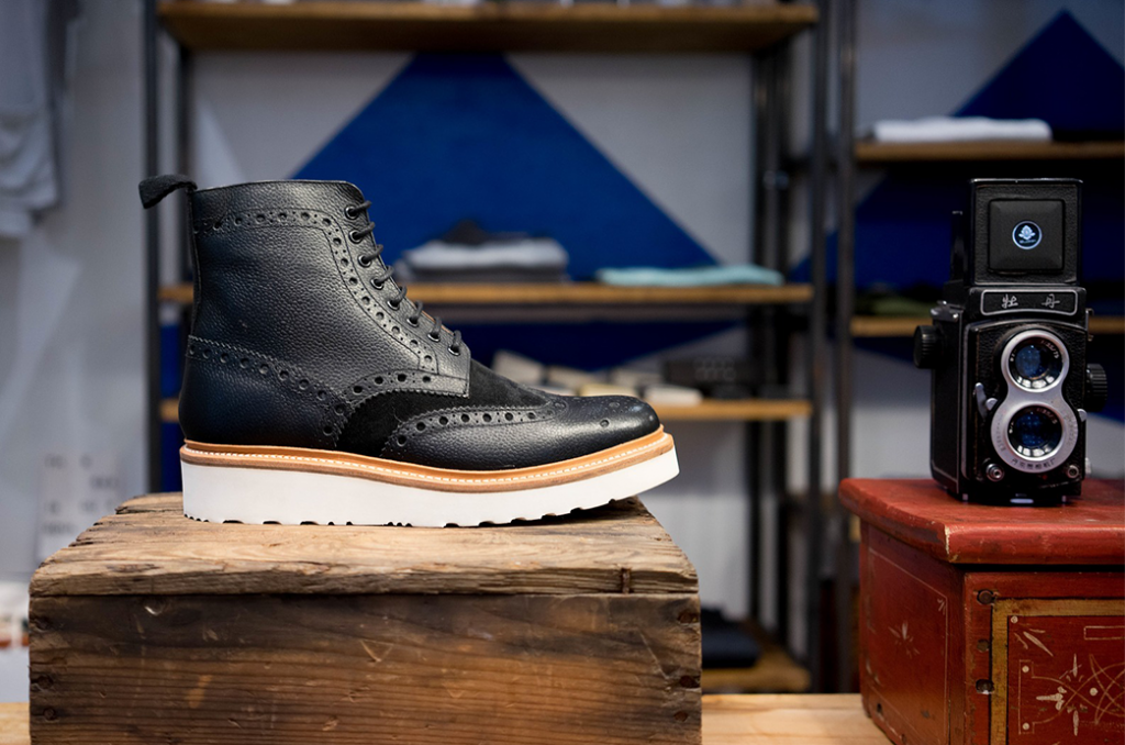Ein schwarzer Schuh steht auf einem Holzklotz. Er wird auf dem Bild so gut dargestellt wie ein Produkt auf einer Produktdetailseite.