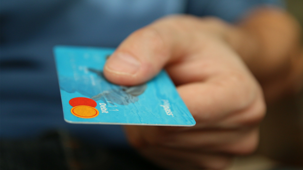 Das Bild zeigt eine Person, die eine Kreditkarte in einer Hand hält. Diese steht im übertragenen Sinn für den Checkout-Prozess im Online-Shop.
