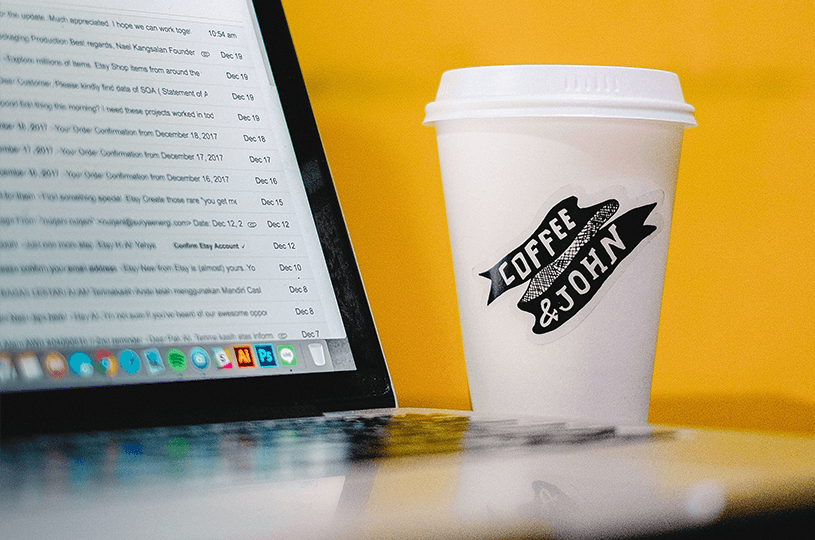 Ein Kaffeebecher und ein Laptop stehen vor einem gelben Hintergrund. Auf dem Laptop ist ein E-Mail-Programm mit vielen ungelesenen E-Mails zu sehen. Um hier herauszustechen, werden E-Mail-Marketing-Tipps benötigt.