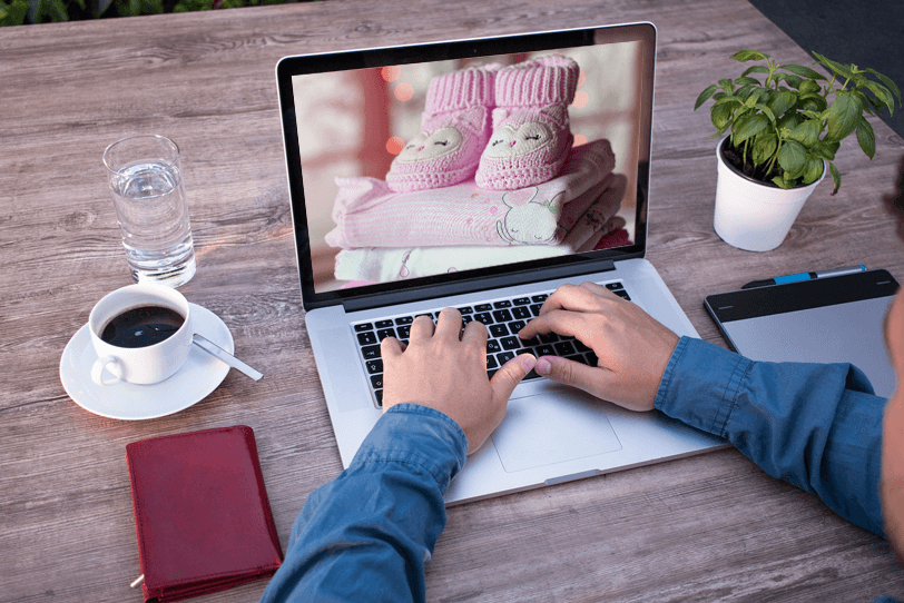 Ein Mann sitzt vor seinem Laptop, auf dem ein Bild von Kinderbekleidung zu sehen ist. Dieses erhält er als Empfehlung in Form einer Lifecycle-E-Mail, die seine aktuellen Bedürfnisse berücksichtigt.